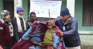Mr Rajendra Kumar Raut (first from right) drapes a blanket around an elderly woman from Rangeli Municipality, Morang while Mr Joseph Soren, Chair of LCWS (second from right) looks on.